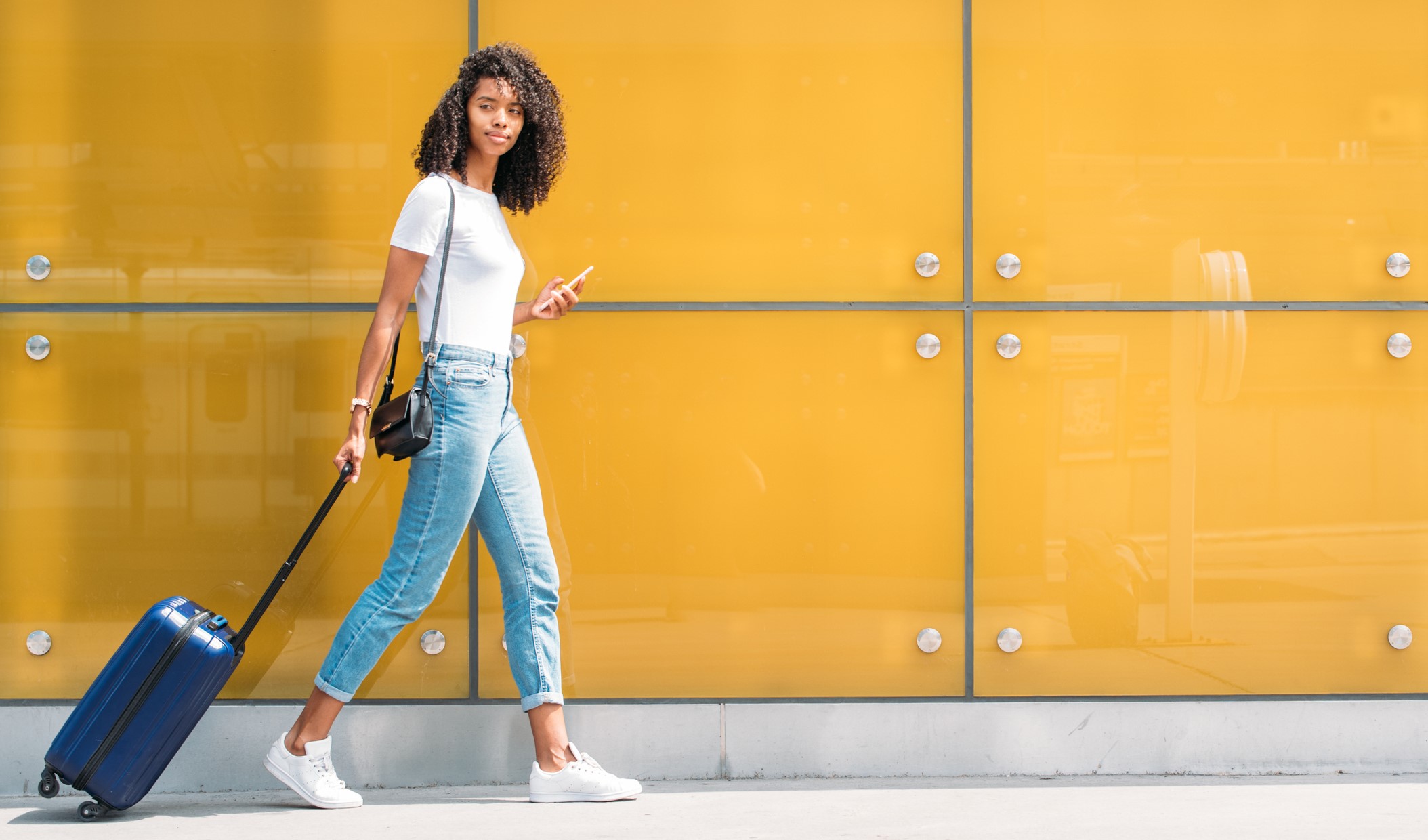 Allied medical professional pulling her luggage down the street while holding her mobile device in the other hand. 